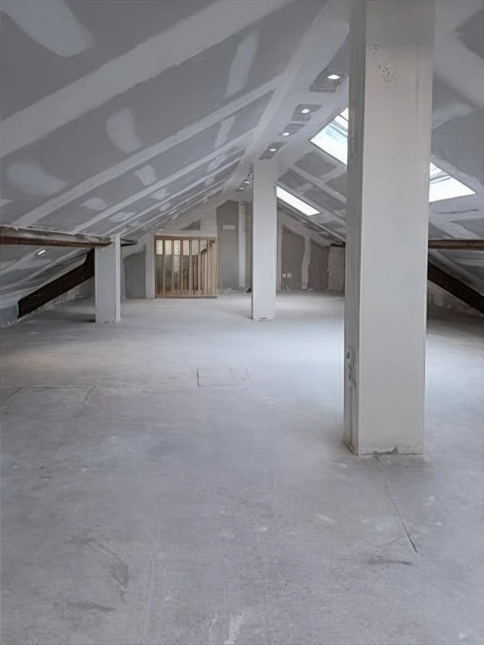 Façade d'une maison individuelle contemporaine en cours de finition avec échafaudage. Le niveau supérieur présente un enduit beige avec encadrements en briques et volets roulants blancs, porte-fenêtre vitrée. Le soubassement arbore un enduit rouge orangé avec petites fenêtres à barreaux. Toiture en tuiles mécaniques, gouttières PVC, terrain enherbé en premier plan.