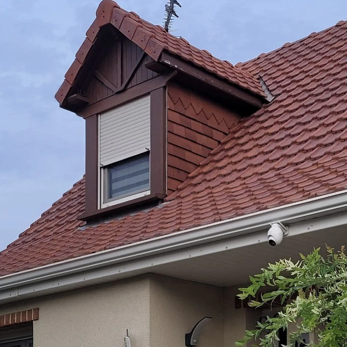 Intérieur résidentiel avec fenêtre de toit ouverte laissant entrer la lumière naturelle. Vue sur toiture extérieure et ciel bleu.