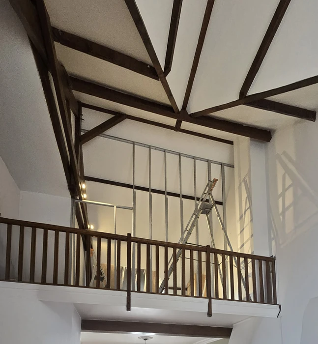 Chantier de rénovation intérieur avec mur en pierre apparente et isolation thermique. Panneaux isolants Rockwool fixés sur ossature métallique, finition placo-plâtre en cours. Sol protégé, outillage de chantier visible.