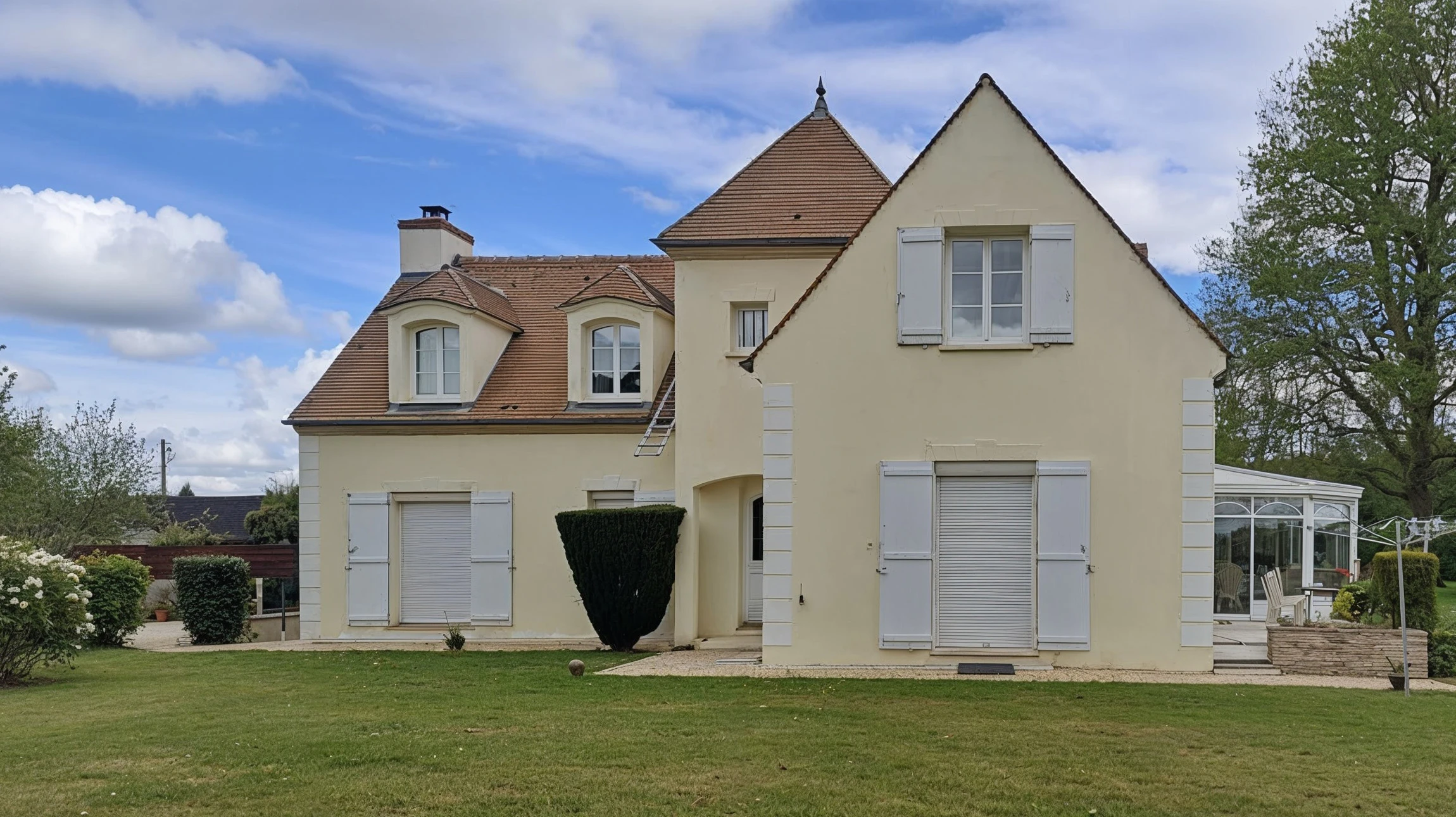 Façade extérieure moderne avec mur en briques peintes vert pâle, porte d'entrée bleue encadrée de blanc, luminaire suspendu doré, plaque d'adresse numérotée, haie verte taillée à la base et trottoir beige.
