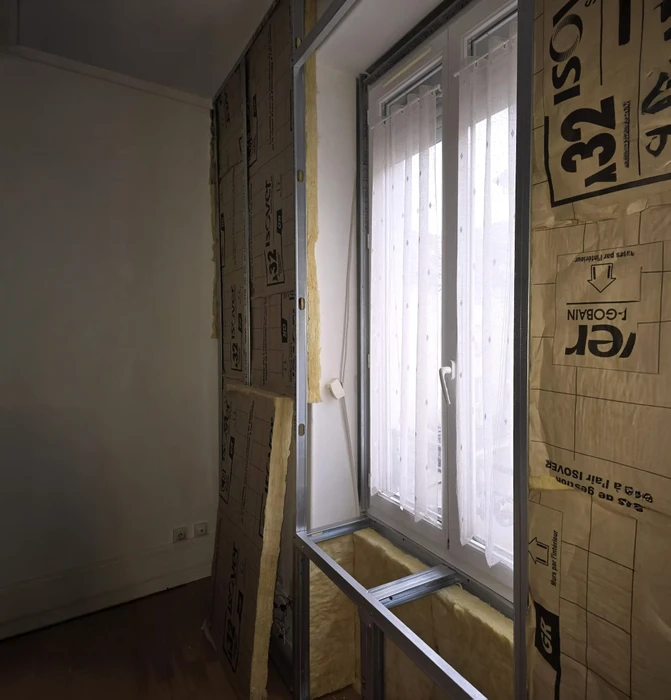 Chantier de rénovation de toiture en extérieur avec deux ouvriers couvreurs installant une membrane d'étanchéité sur charpente apparente. Présence d'isolant thermique jaune entre les chevrons.