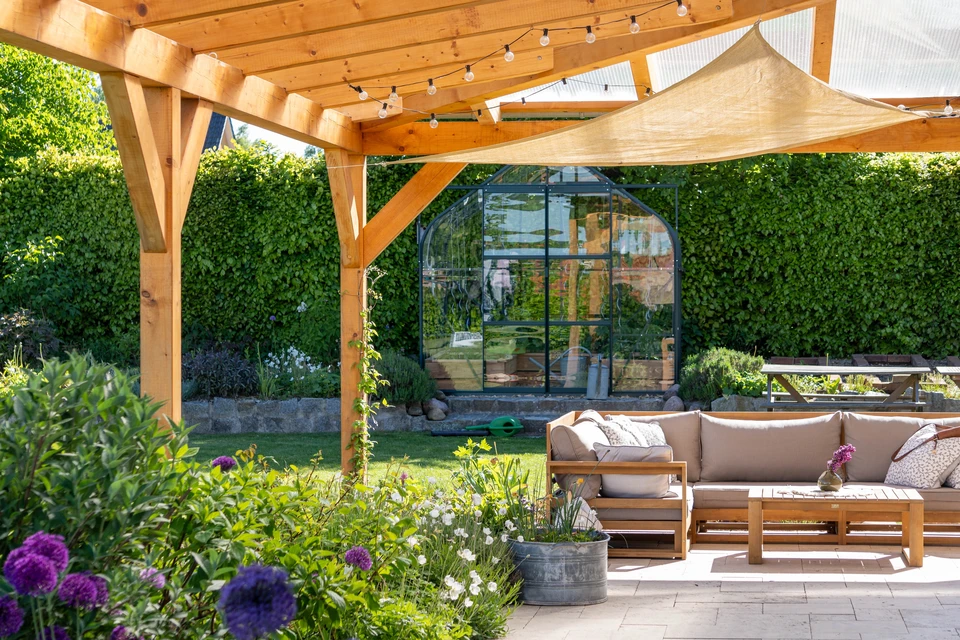 Vue de devant d'une joyeuse famille assise à l'extérieur sur la terrasse d'une maison de campagne. Un élégant jeune couple le week-end s'installe et jouit d'une vue sur la nature sur la terrasse de leur maison moderne avec des fenêtres panoramiques.