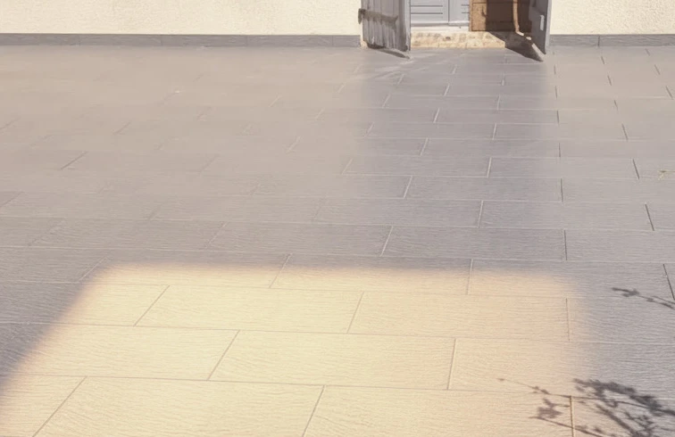 Artisan menuisier travaillant en extérieur, façonnant une pièce de bois avec un ciseau à bois et maillet. Copeaux et poussière de bois voltigent dans l'air. Établi en bois massif avec plusieurs planches de bois brut. Ciseau à bois à manche bleu, technique de mortaisage ou tenonnage. Essence de bois clair, travail de charpenterie traditionnelle.